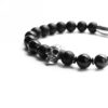 Czarna bransoletka z kulkami i metalową czaszką na białym tle.