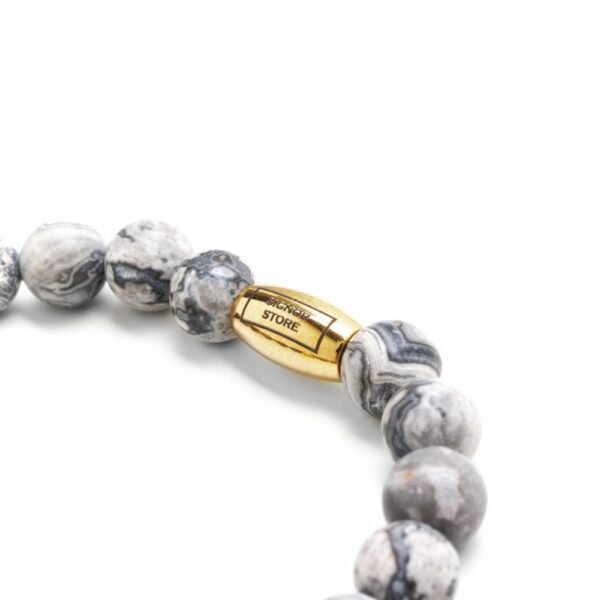 Bransoletka z szarymi kamiennymi koralikami i złotą ozdobą.