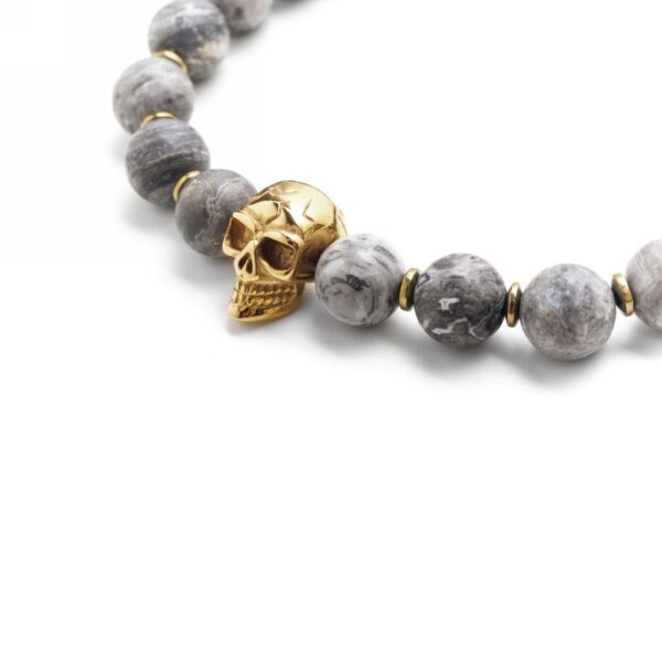 Bransoletka z szarymi kamieniami i złotym motywem czaszki.