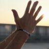 Dłonie uniesione w stronę słońca, na jednej z nich bransoletka z literami tworzącymi słowo TATA.