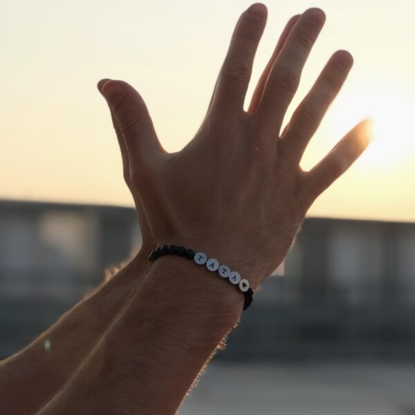 Dłonie uniesione w stronę słońca, na jednej z nich bransoletka z literami tworzącymi słowo TATA.