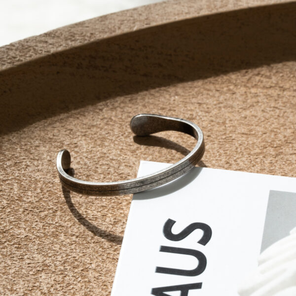 Srebrna bransoletka leżąca na korkowej powierzchni obok białej kartki z napisem.