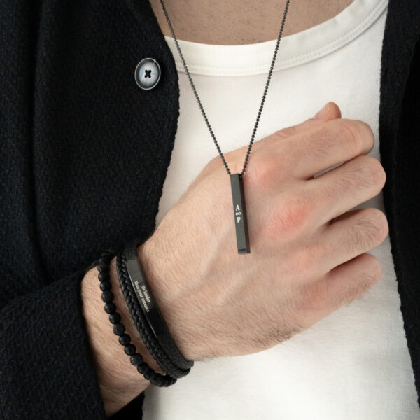 Mężczyzna w białej koszulce i czarnej marynarce z czarnym naszyjnikiem i bransoletkami.