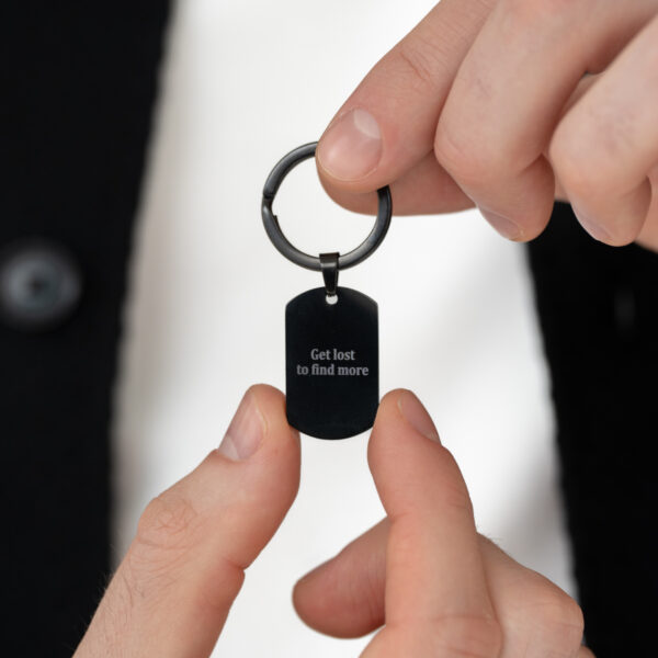 Osoba trzymająca brelok z napisem 'Get lost to find more'.