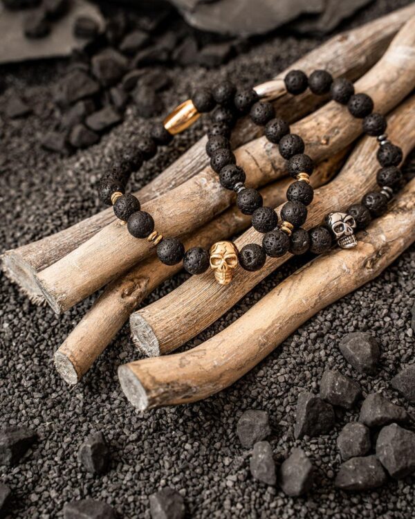 Stylowe bransoletki z czarnych koralików z ozdobami w kształcie czaszek na tle drewnianych patyczków.