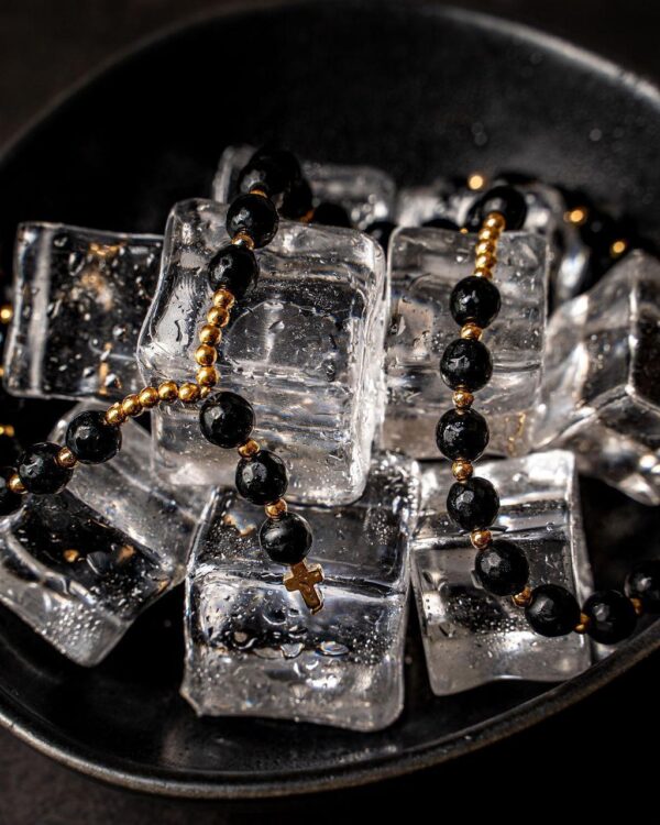 Miseczka z kostkami lodu i czarnym naszyjnikiem z koralików i krzyżem.