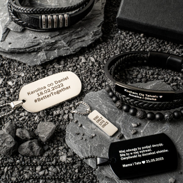 Bransoletki i zawieszki z grawerowanymi napisami na kamiennej powierzchni.