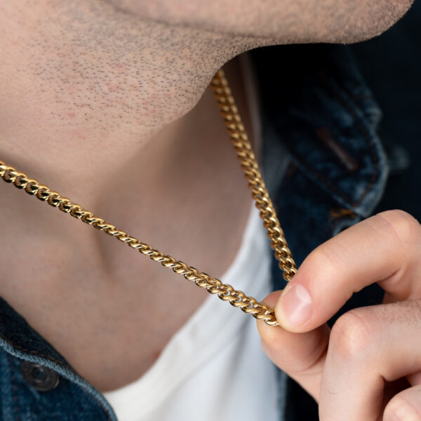 Zbliżenie na szyję osoby noszącej złoty naszyjnik.