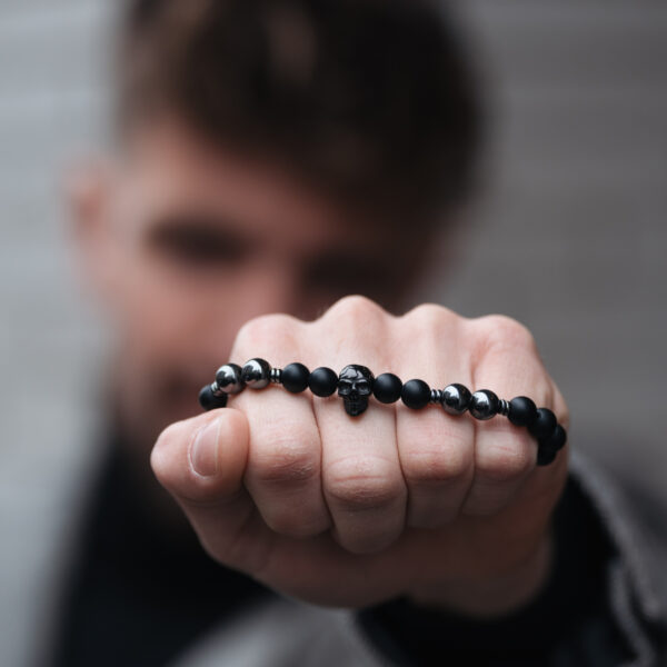 Mężczyzna trzymający bransoletkę z czarnymi koralikami i czaszką