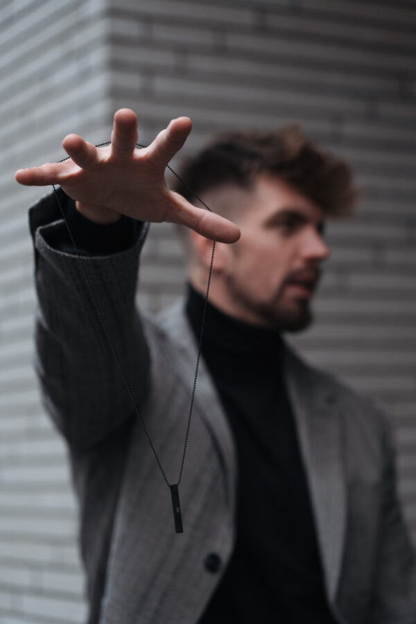 Mężczyzna w szarym garniturze trzymający naszyjnik na wyciągniętej dłoni.