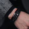 Męska ręka z elegancką, czarną skórzaną bransoletką z metalowymi elementami.