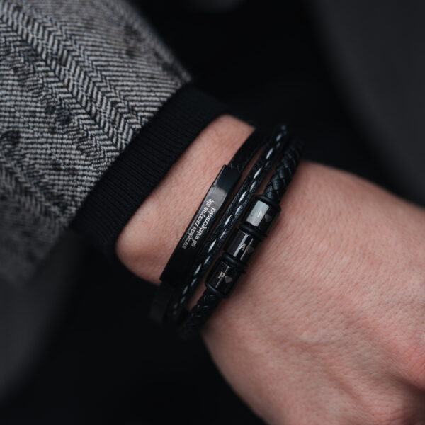 Męska ręka z elegancką, czarną skórzaną bransoletką z metalowymi elementami.