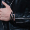 Męska ręka w czarnej skórzanej kurtce z czarnymi bransoletkami.