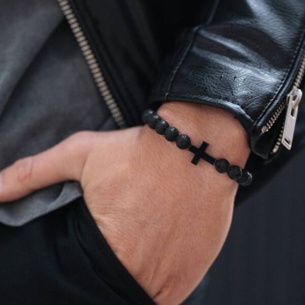 Bransoletka z czarnymi paciorkami i krzyżem na nadgarstku z ręką w kieszeni.