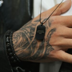 Ręka z tatuażem trzymająca naszyjnik z napisem 'wybieraj ludzi, którzy wybierają Ciebie'.