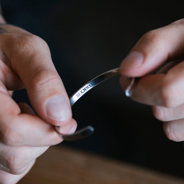 Osoba trzymająca srebrną bransoletkę z wygrawerowanymi rzymskimi cyframi.