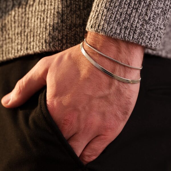 Męska ręka z bransoletką, włożona do kieszeni spodni.