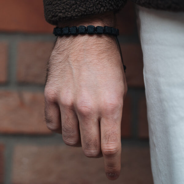 Zbliżenie na męską rękę z czarną bransoletką na tle ceglanej ściany.