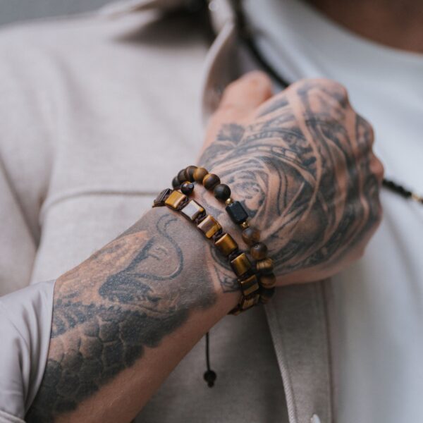 Ręka z tatuażami nosząca dwie bransoletki z kamieni tygrysiego oka.