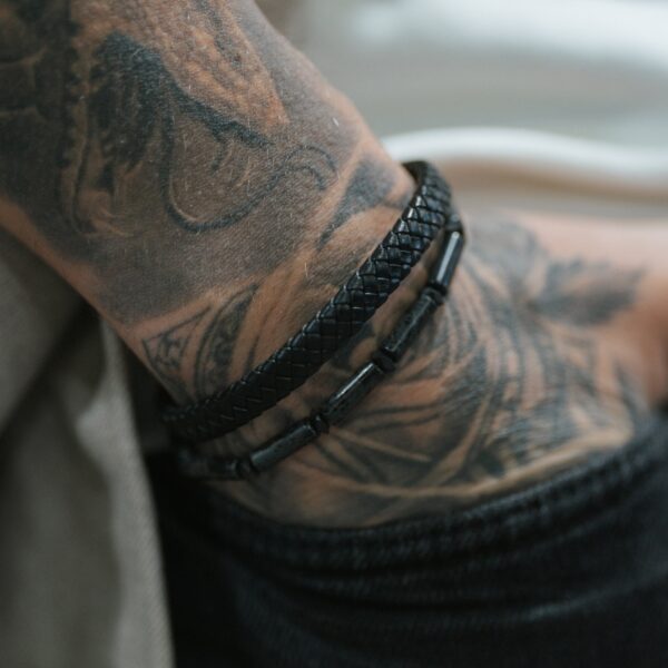 Tatuaż na ręce z czarną, plecioną bransoletką.