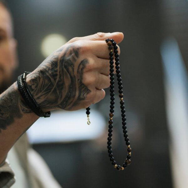 Osoba z tatuażem na ręce trzyma sznur czarnych koralików.