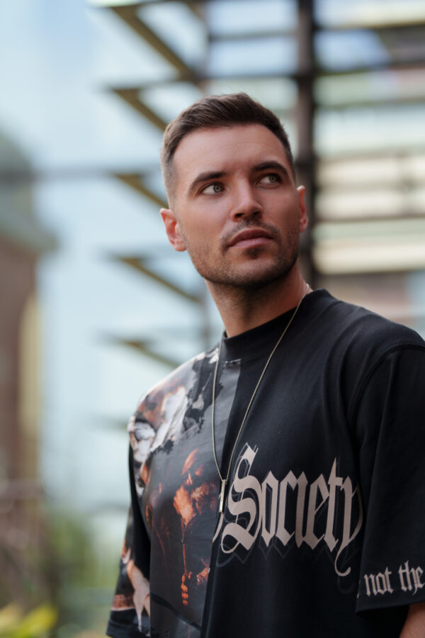 Mężczyzna patrzący w dal w czarnej koszulce z napisem 'Society'.