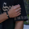 Ręka w czarnej koszulce z napisem i bransoletką z czarnych koralików oraz pierścionkiem