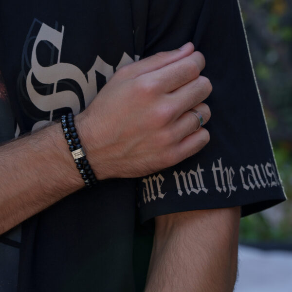 Ręka w czarnej koszulce z napisem i bransoletką z czarnych koralików oraz pierścionkiem