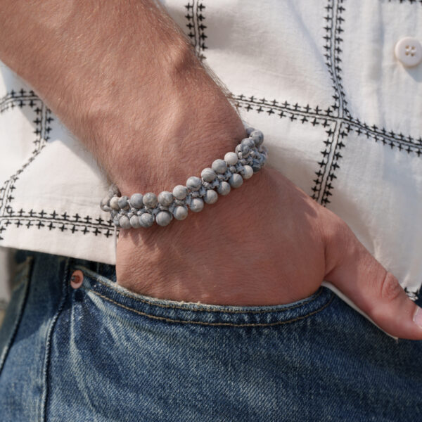 Osoba nosząca bransoletkę z kamieniami na nadgarstku, z ręką włożoną do kieszeni dżinsów.