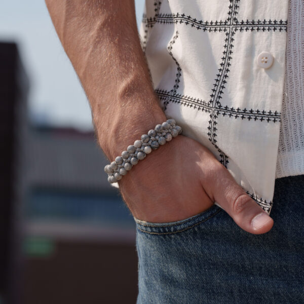 Męska ręka z bransoletką z kamieniami, włożona do kieszeni dżinsów.