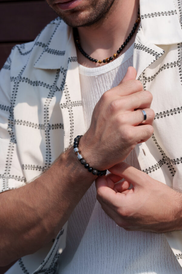 Mężczyzna w koszuli prezentuje bransoletkę i naszyjnik.