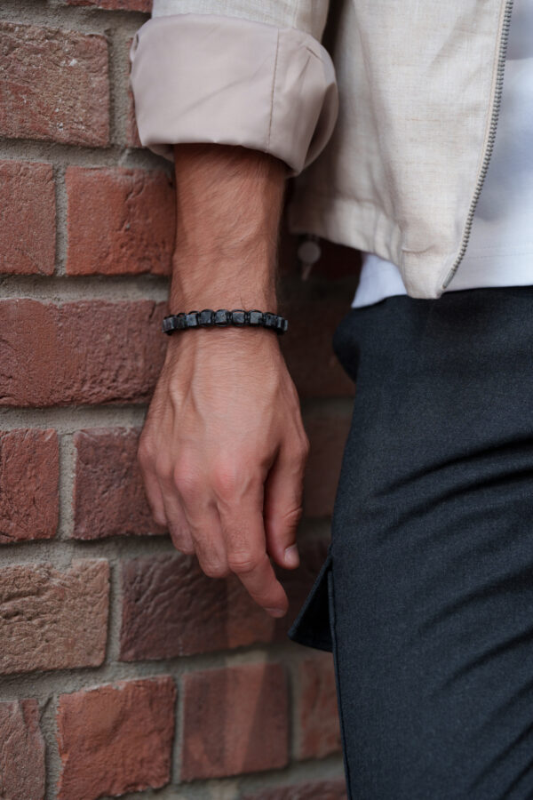 Zbliżenie na męską rękę z bransoletką na tle ceglanej ściany.