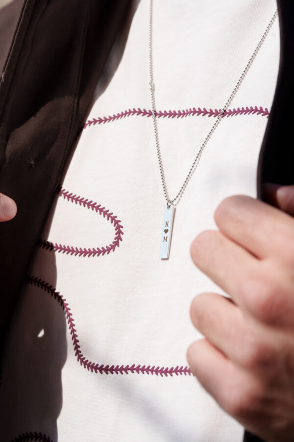 Biały T-shirt z fioletowym wzorem i naszyjnikiem z literami K i M.