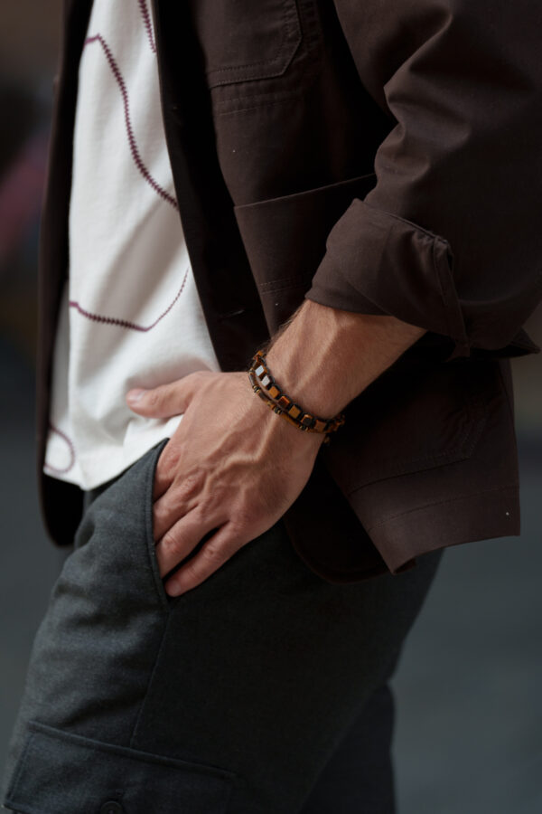 Mężczyzna w brązowej kurtce i białej koszulce wkłada rękę do kieszeni.