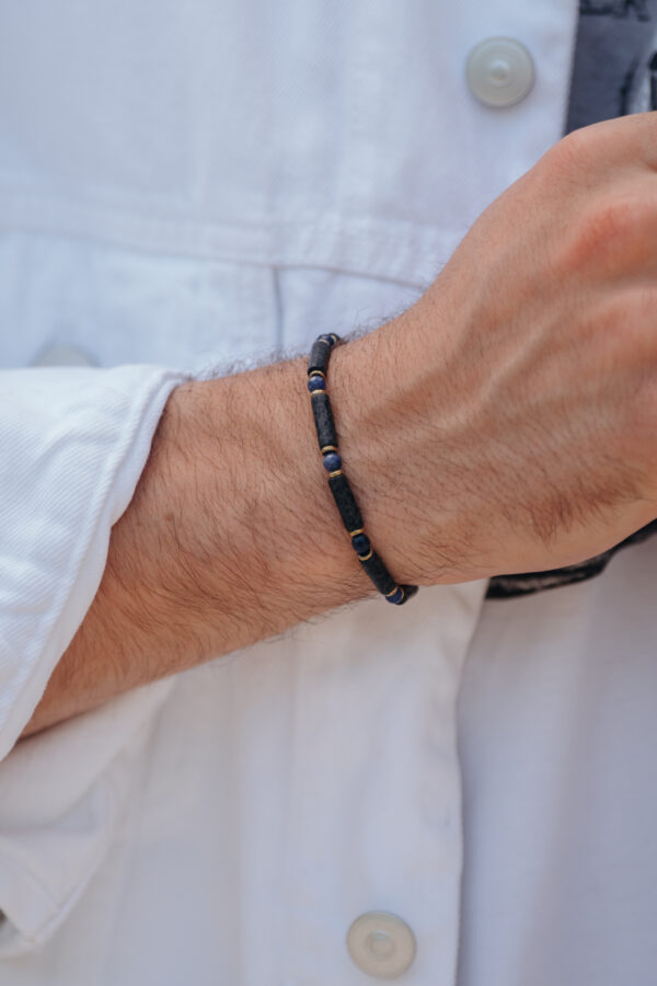 Męska ręka w białej koszuli z czarną bransoletką.