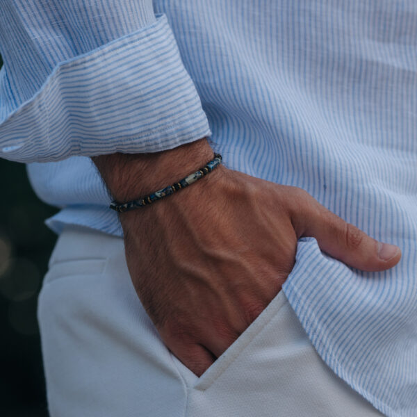 Mężczyzna w pasiastej koszuli z ręką w kieszeni i bransoletką na nadgarstku.