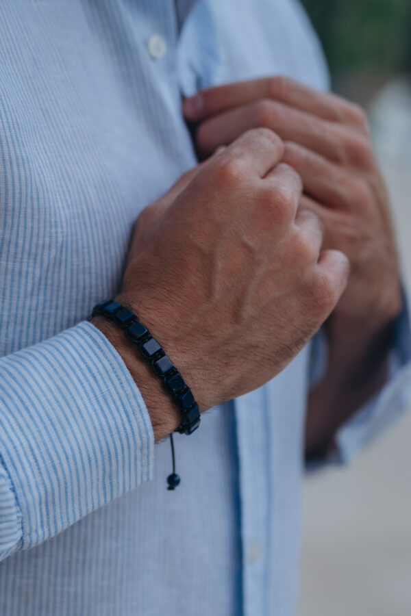 Mężczyzna zapinający guziki koszuli, noszący czarną bransoletkę.
