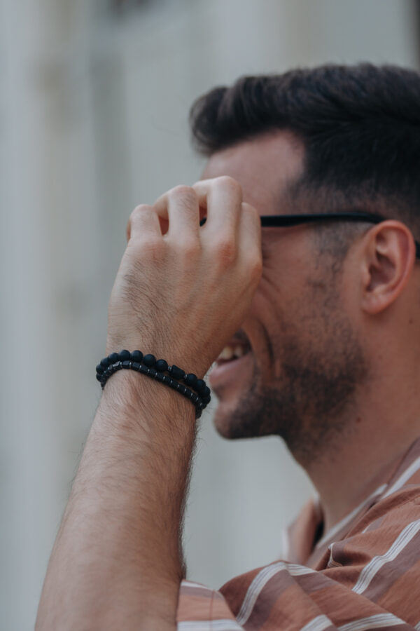 Mężczyzna w okularach uśmiechający się, z bransoletkami na ręce