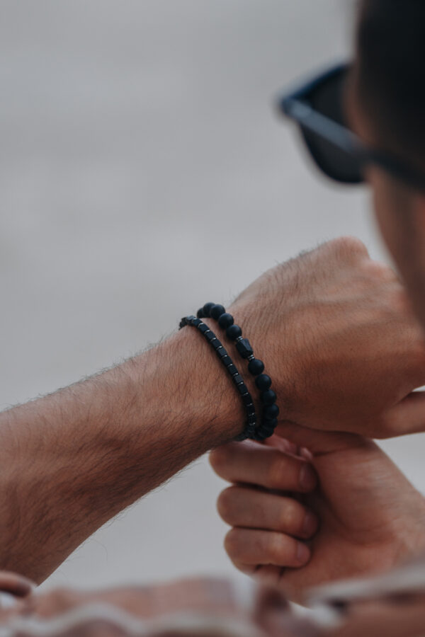 Zbliżenie na męski nadgarstek ozdobiony czarnymi bransoletkami.