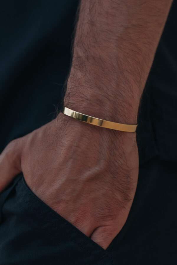 Ręka z prostą, złotą bransoletką na nadgarstku.