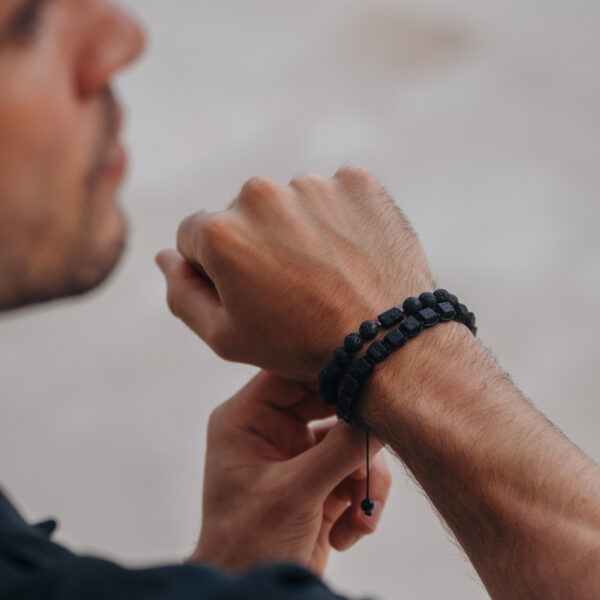 Mężczyzna zakładający na nadgarstek bransoletkę z czarnych koralików.