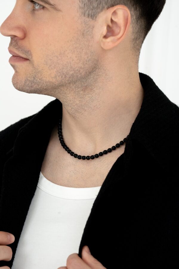 Mężczyzna w białej koszulce i czarnym naszyjniku z koralików.