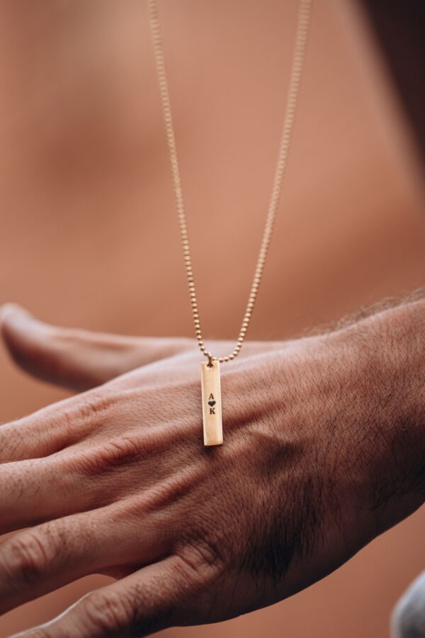 Złoty naszyjnik z grawerem 'A <3 K' na tle dłoni.