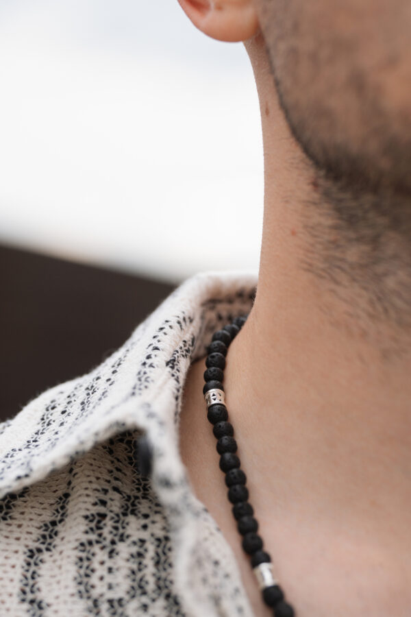 Zbliżenie na naszyjnik z czarnymi koralikami na szyi mężczyzny.