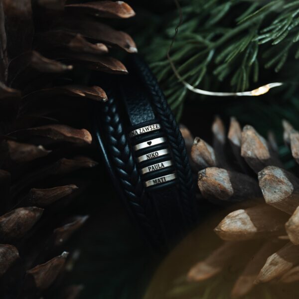 Skórzana bransoletka z metalowymi elementami w otoczeniu szyszek i zielonych gałązek.