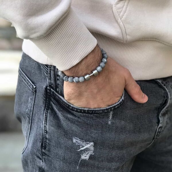 Osoba w szarych dżinsach i jasnej bluzie nosząca bransoletkę z szarymi koralikami.