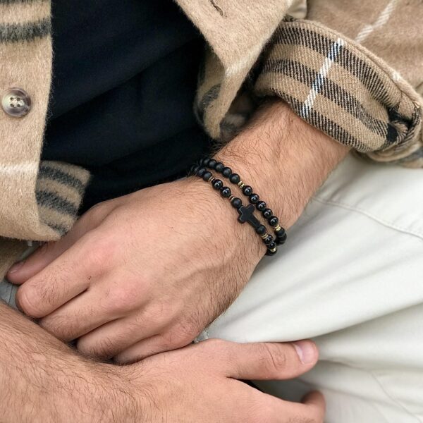 Zbliżenie na męską dłoń z czarną bransoletką z krzyżykiem.