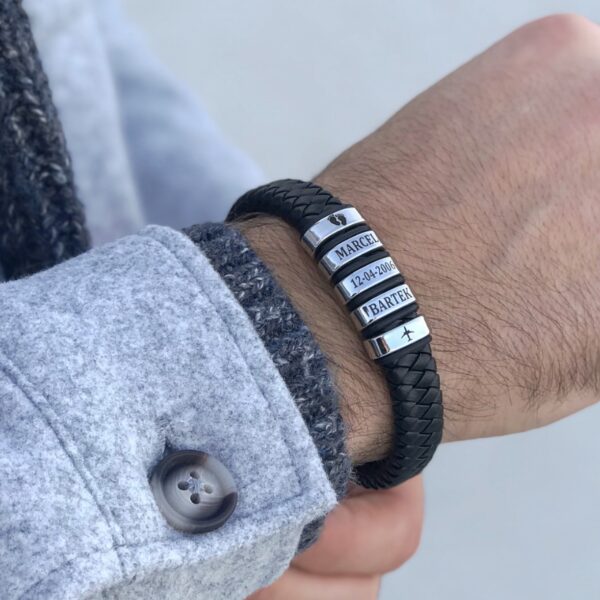 Męska bransoletka z czarnego plecionego materiału z metalowymi, grawerowanymi koralikami na nadgarstku.