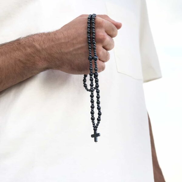 Osoba trzymająca czarny różaniec z krzyżem.