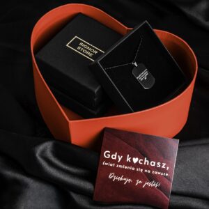 Czarne opakowanie z łańcuchem i zawieszką w kształcie nieśmiertelnika w czerwonym pudełku serce oraz kartka z napisem 'Gdy kochasz, świat zmienia się na zawsze. Dziękuję, że jesteś'.", "title": "Zestaw prezentowy z czarną biżuterią i romantyczną kartką."